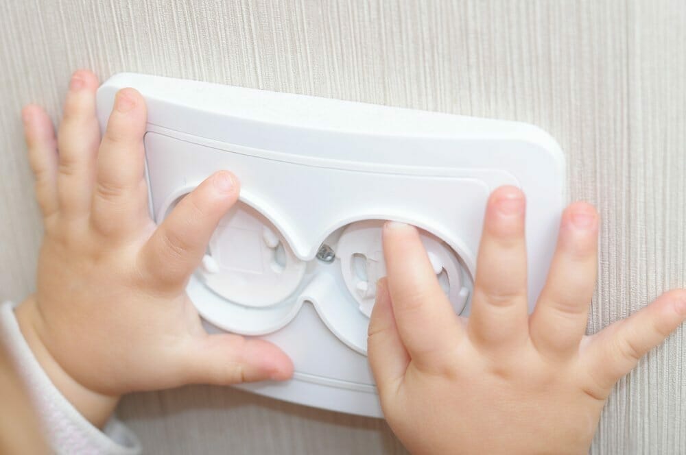 Manos de un bebe sobre un tomacorriente doble protegido con tapas de seguridad.