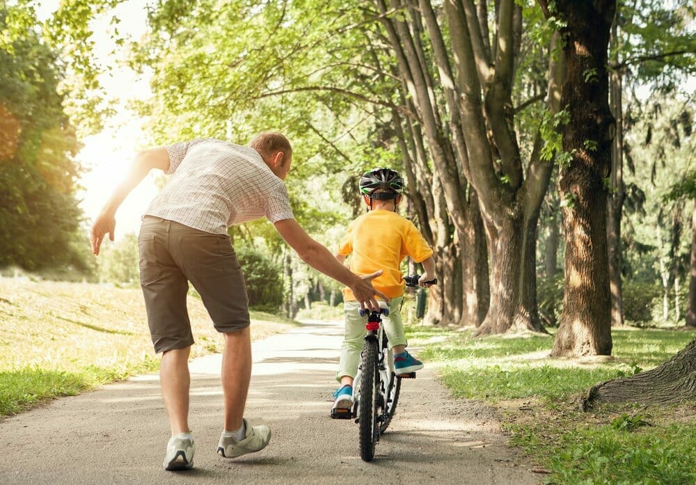 Padre ayuda a su hijo a montar en bicicleta.