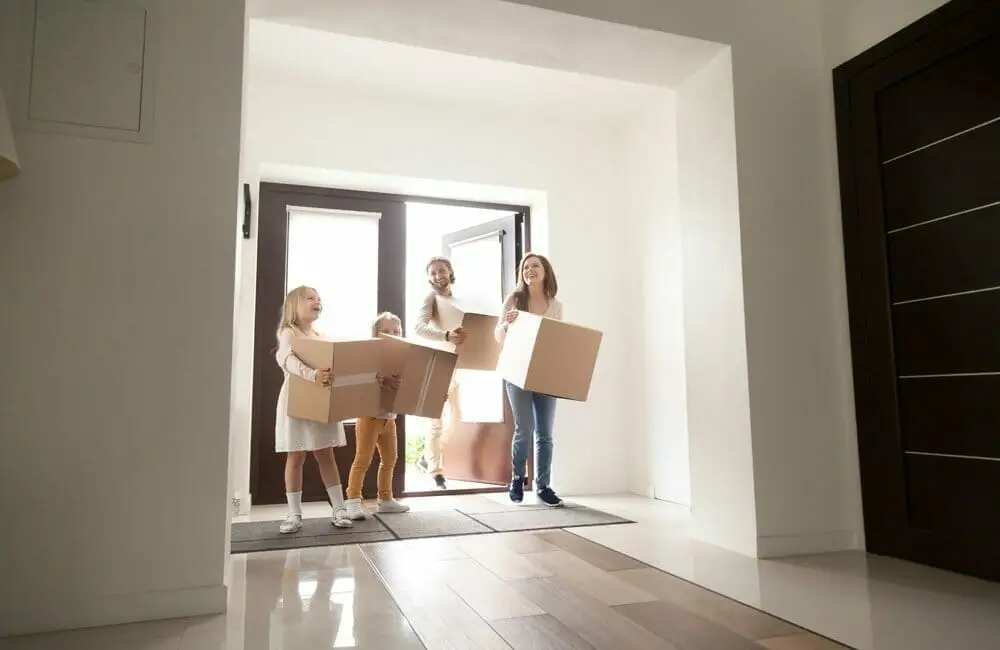 Miembros de una familia mudándose a su nueva casa con cajas de cartón en sus manos.