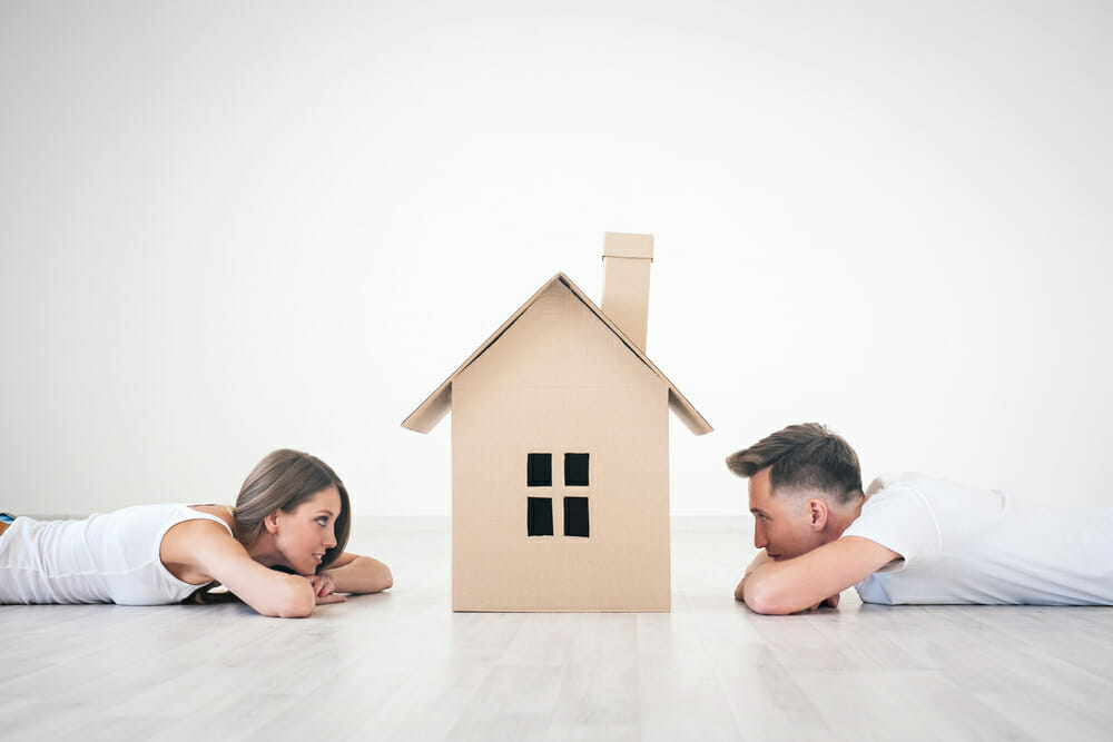 Hombre y mujer tumbados en el suelo miran la maqueta de una casa.