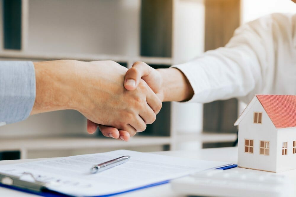 Un agente de bienes raíces y un cliente se dan la mano después de cerrar un contrato de compraventa de una casa.