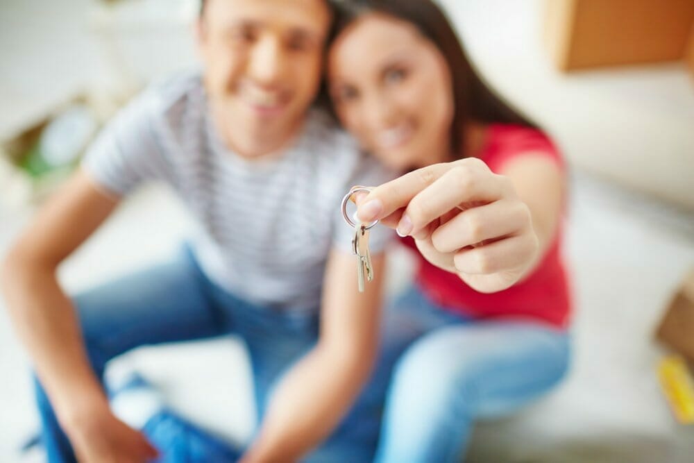 Mujer dándole un abrazo a su novio con las llaves de su nueva casa en su mano.