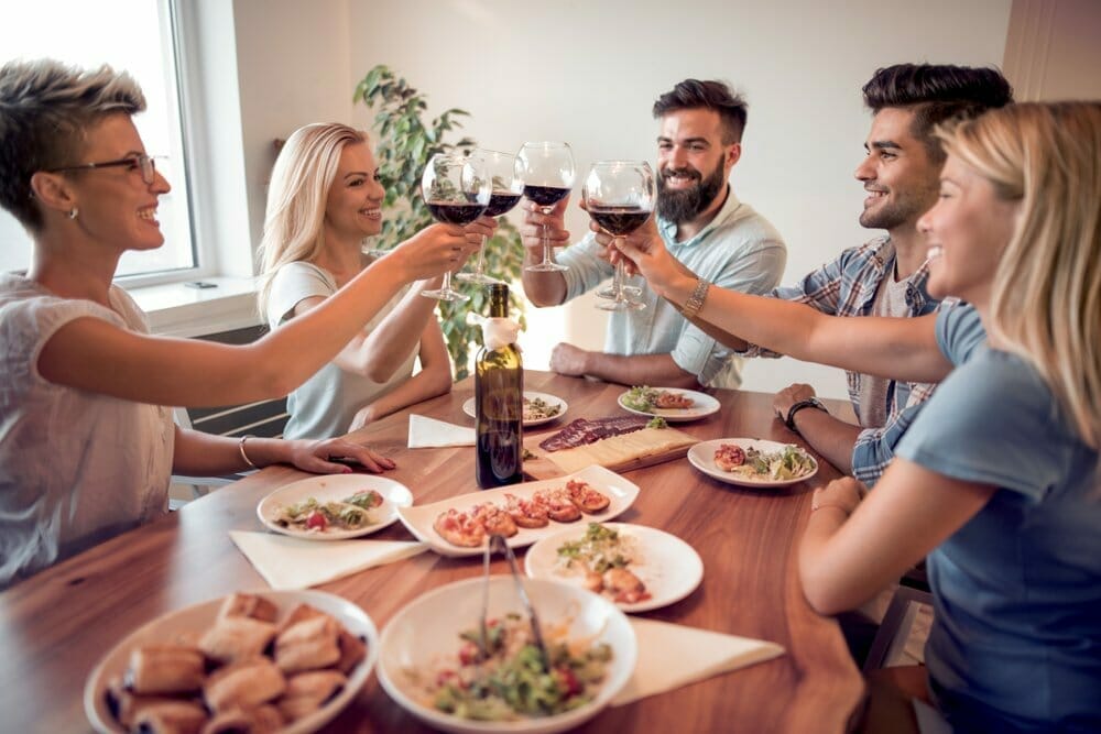 2 hombres y 3 mujeres sentados a la mesa brindan con copas de vino durante una reunión familiar.