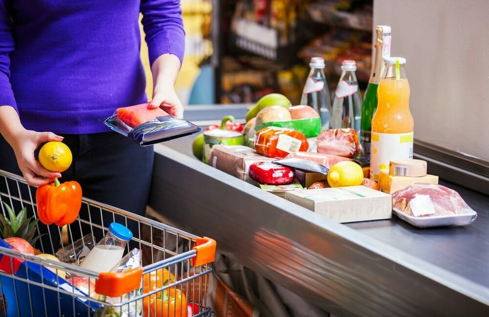 Mujer saca los productos del carrito de compra y los coloca sobre el mostrador del supermercado.