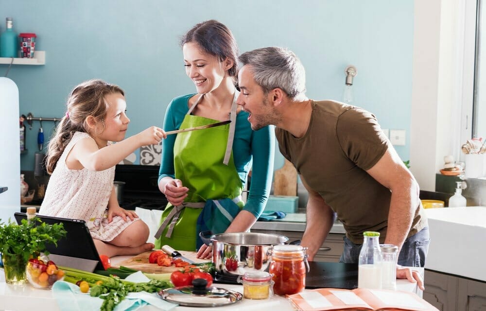 Madre e hija preparan recetas fáciles en casa y el padre está probando la comida.