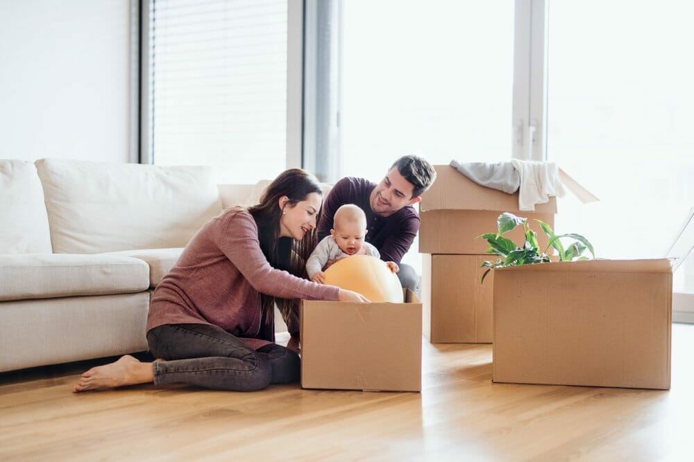 Hombre y mujer desempaquetan las cajas de cartón con sus cosas después de mudarse. El niño coge la pelota de la caja.
