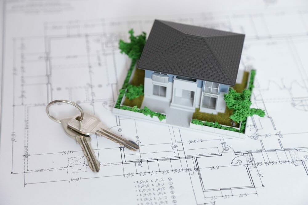 Maqueta de una casa y llaves sobre un plano arquitectónico.
