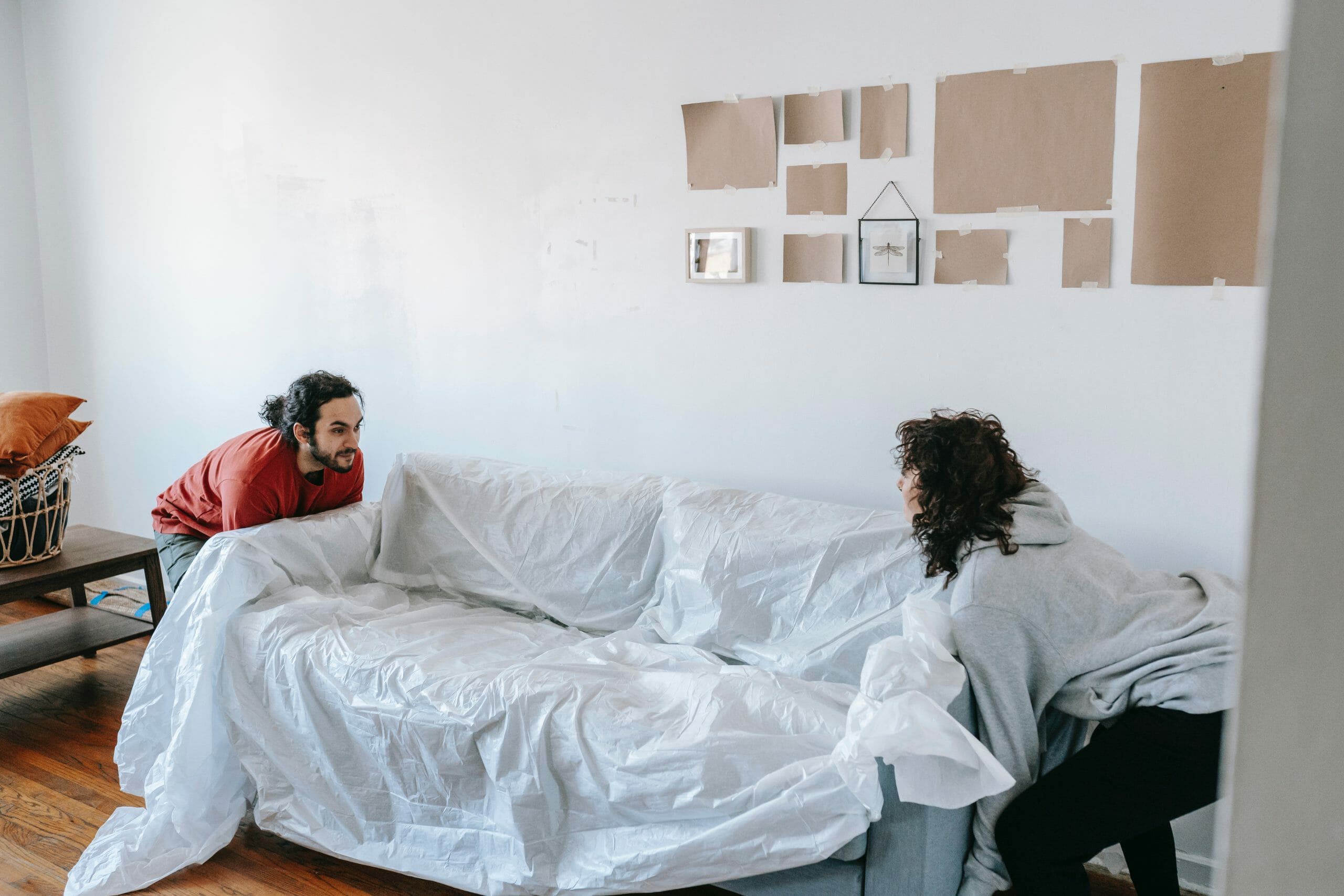 Pareja levantando sofá de la sala protegido con sabana blanca para decorar la pared