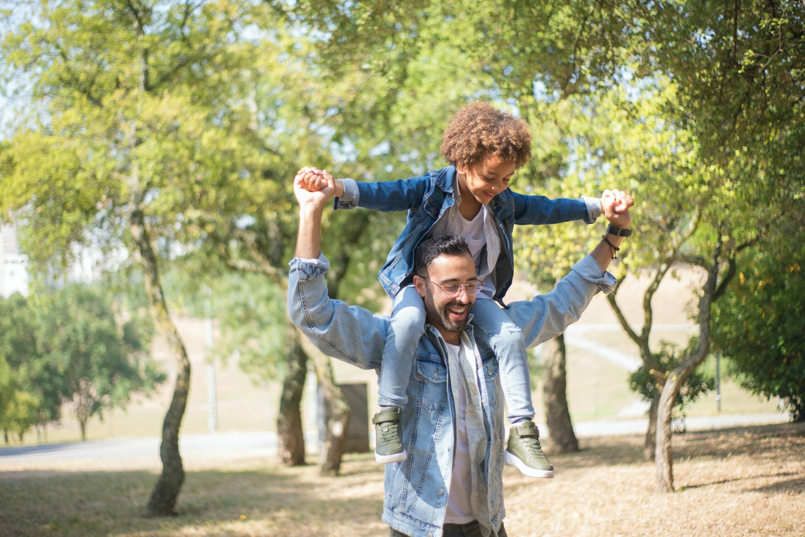 Padre e hijo en hombros sonriendo y felices al aire libre.