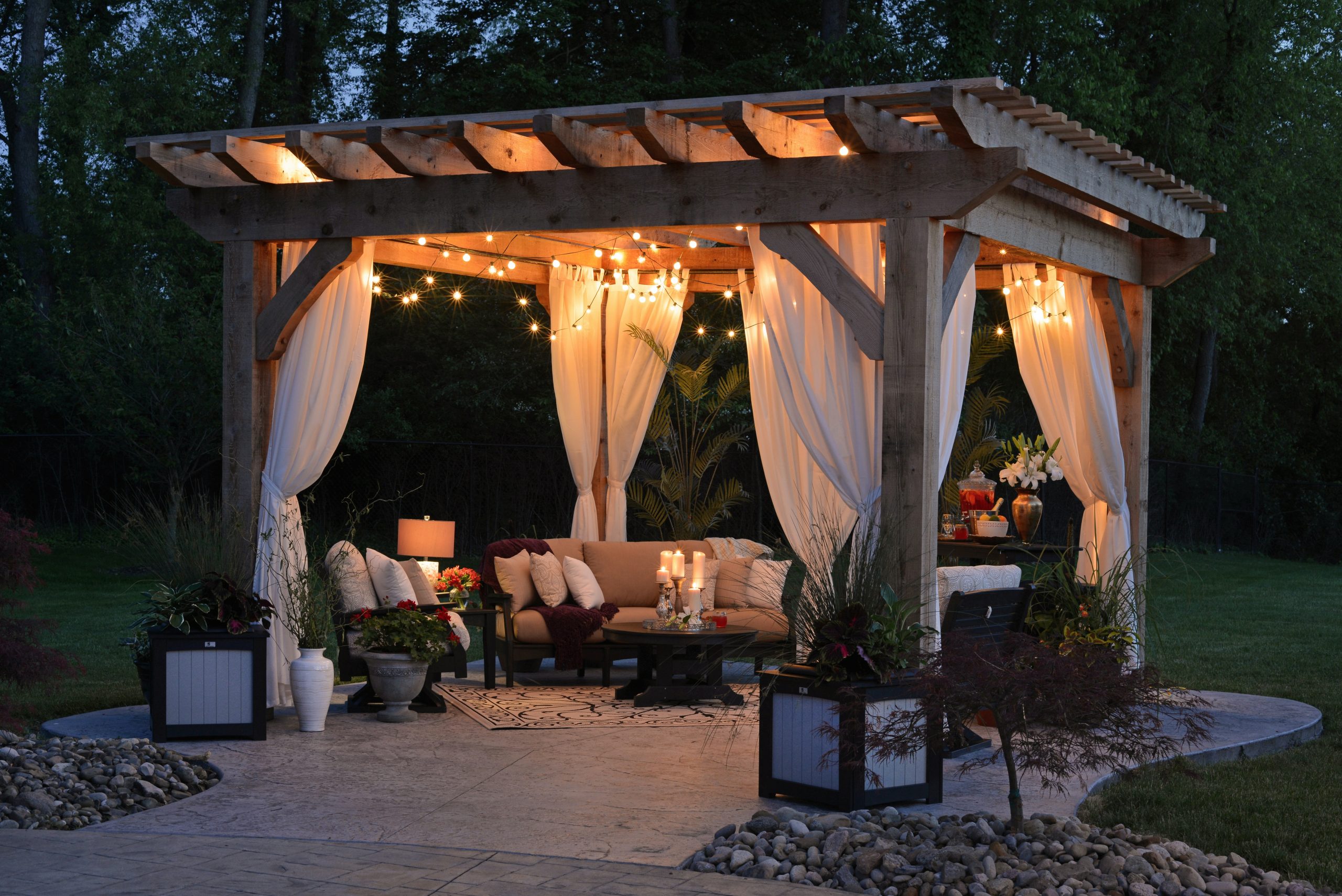 Patio con gazebo iluminado con luces decorativas y velas, rodeado de sillas y asientos con cojines decorativos