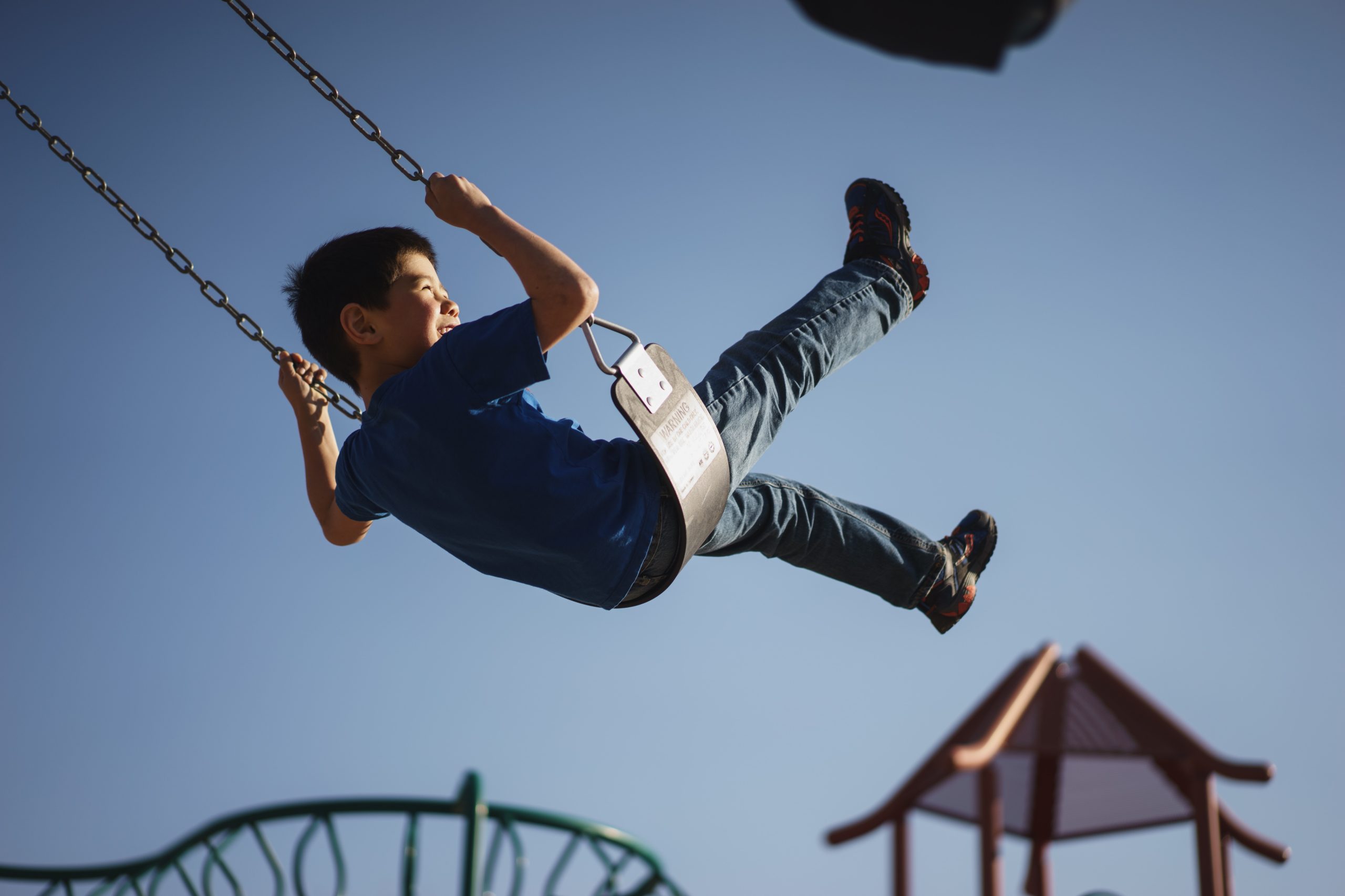 Niño columpiándose mientras juega en área recreativa infantil.