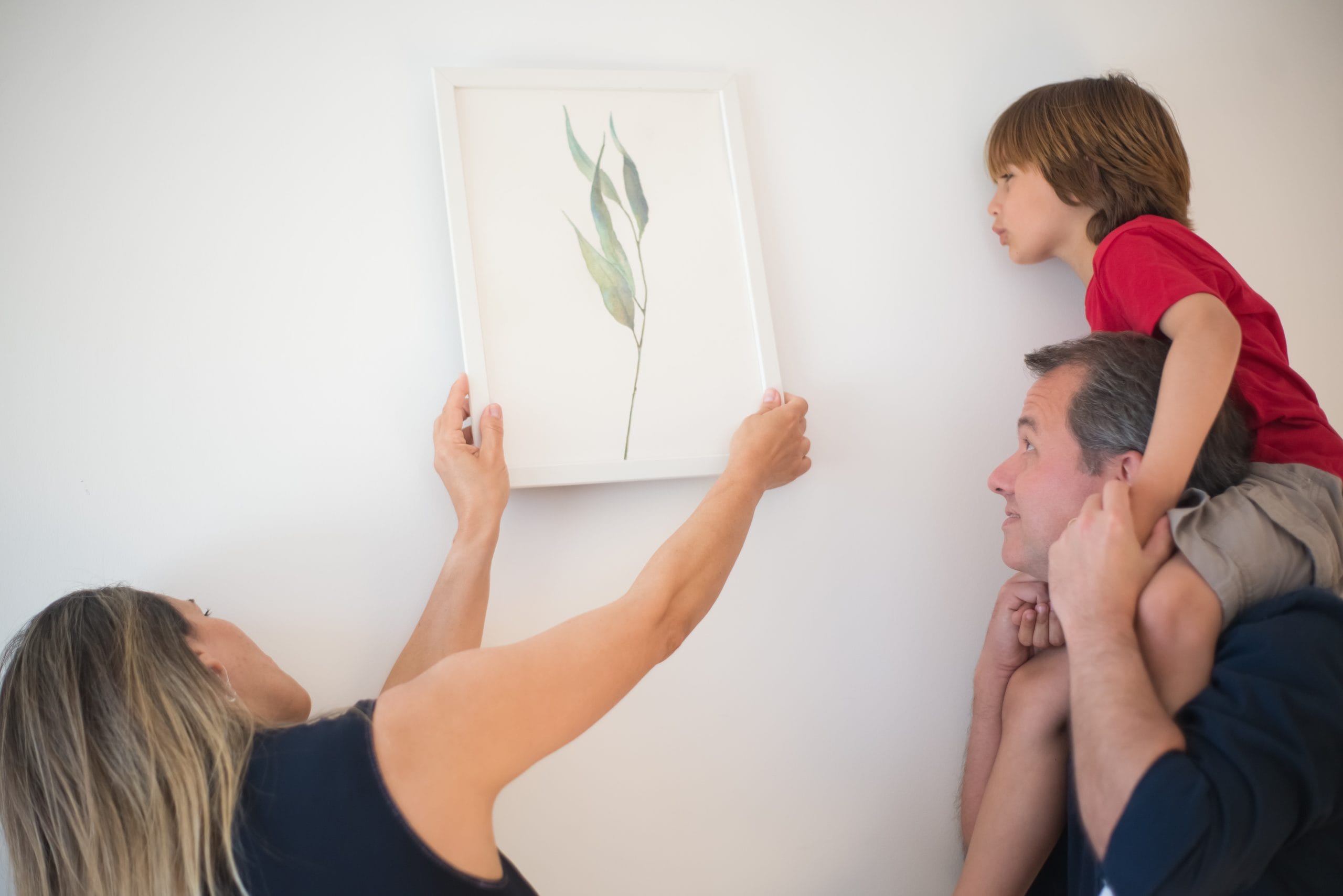 Familia colgando un cuadro minimalista sobre una pared de su hogar