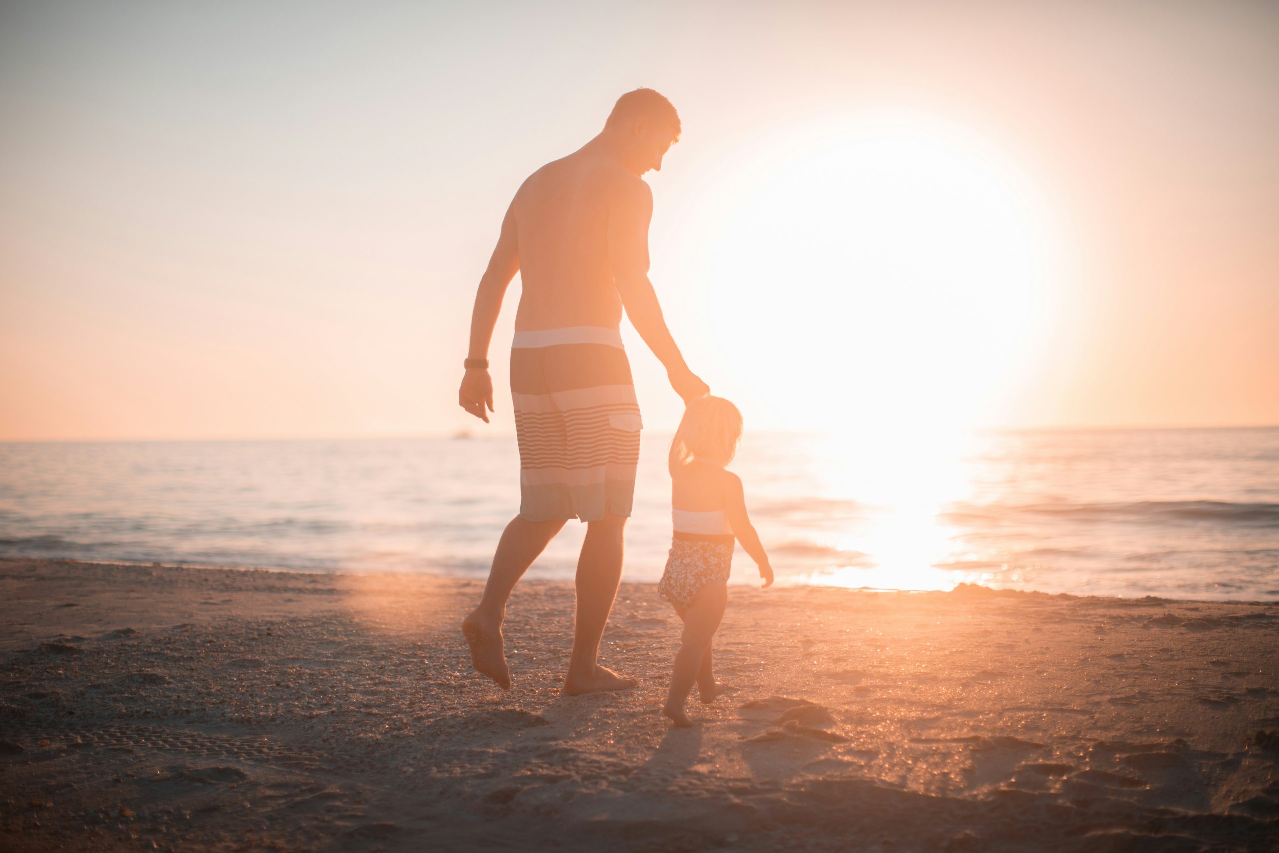Padre e hija tomados de la mano caminando en la playa.