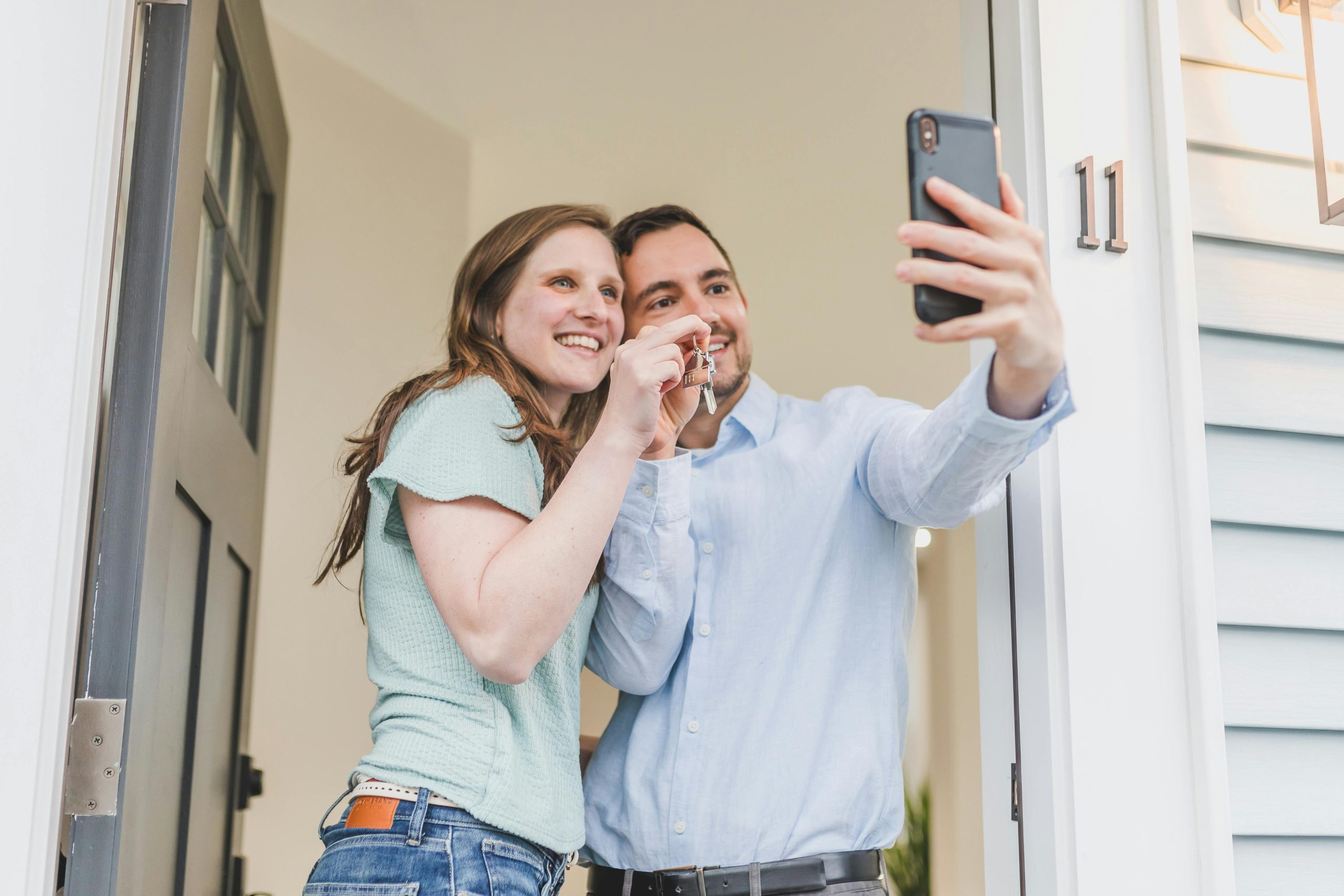 Pareja tomándose una selfie mientras sostiene la llave de su nuevo hogar.