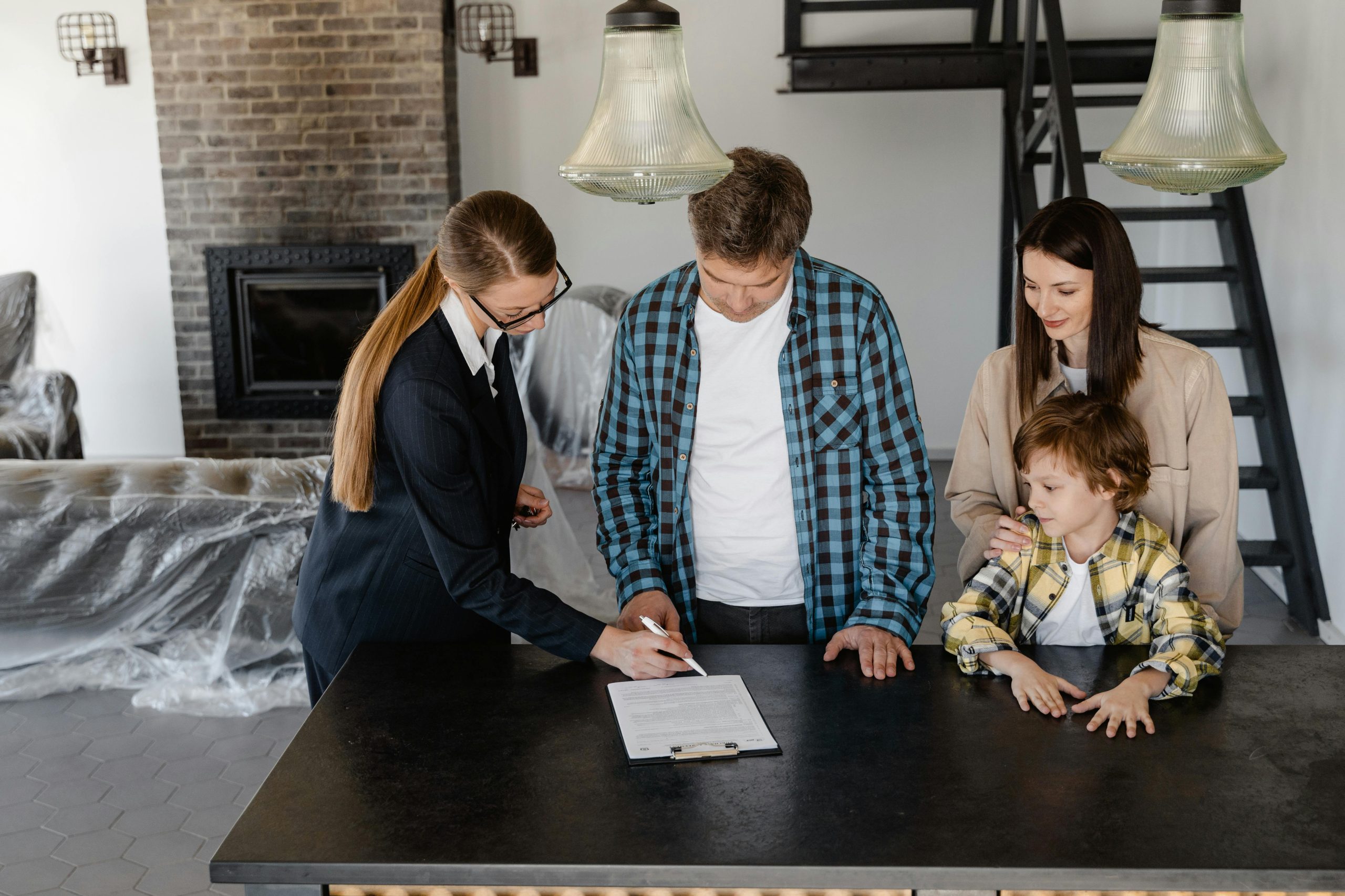 Padre de familia junto a esposa e hijo firmando escritura de su nuevo hogar frente a agente de bienes raíces.