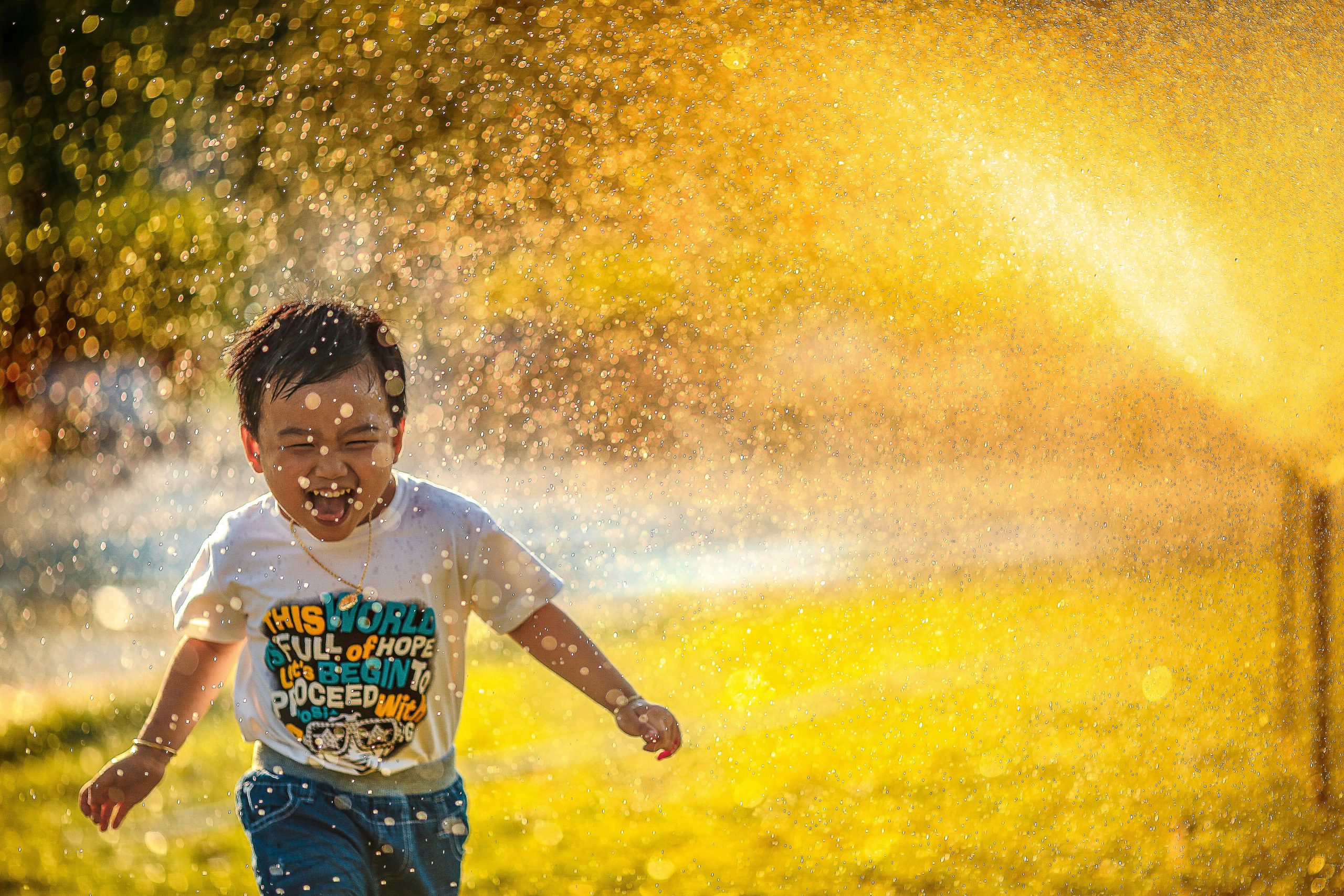 Un niño pequeño jugando y corriendo a través de un chorro de agua en un parque.