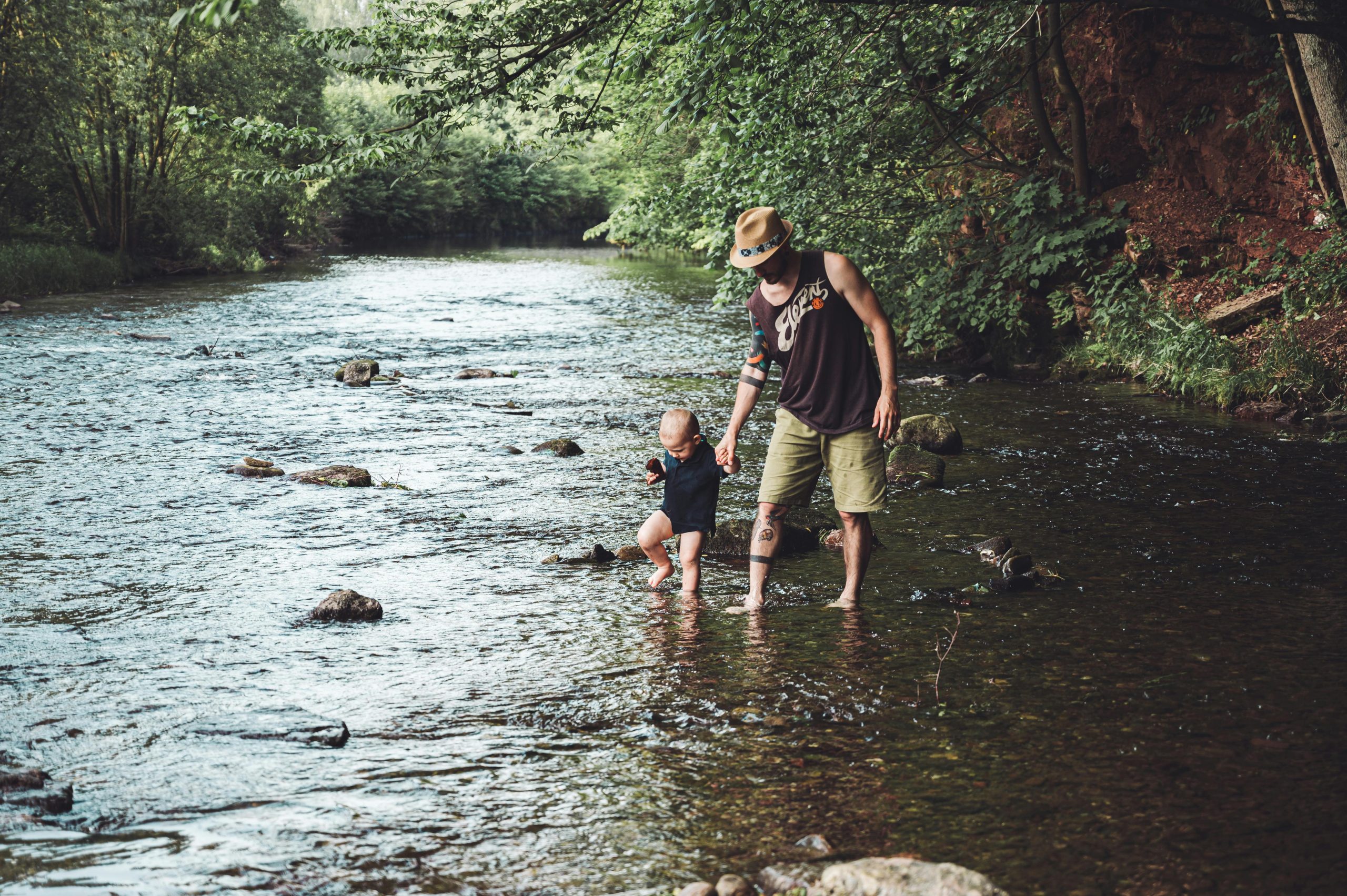 Padre con su hijo pequeño de la mano explorando un río.
