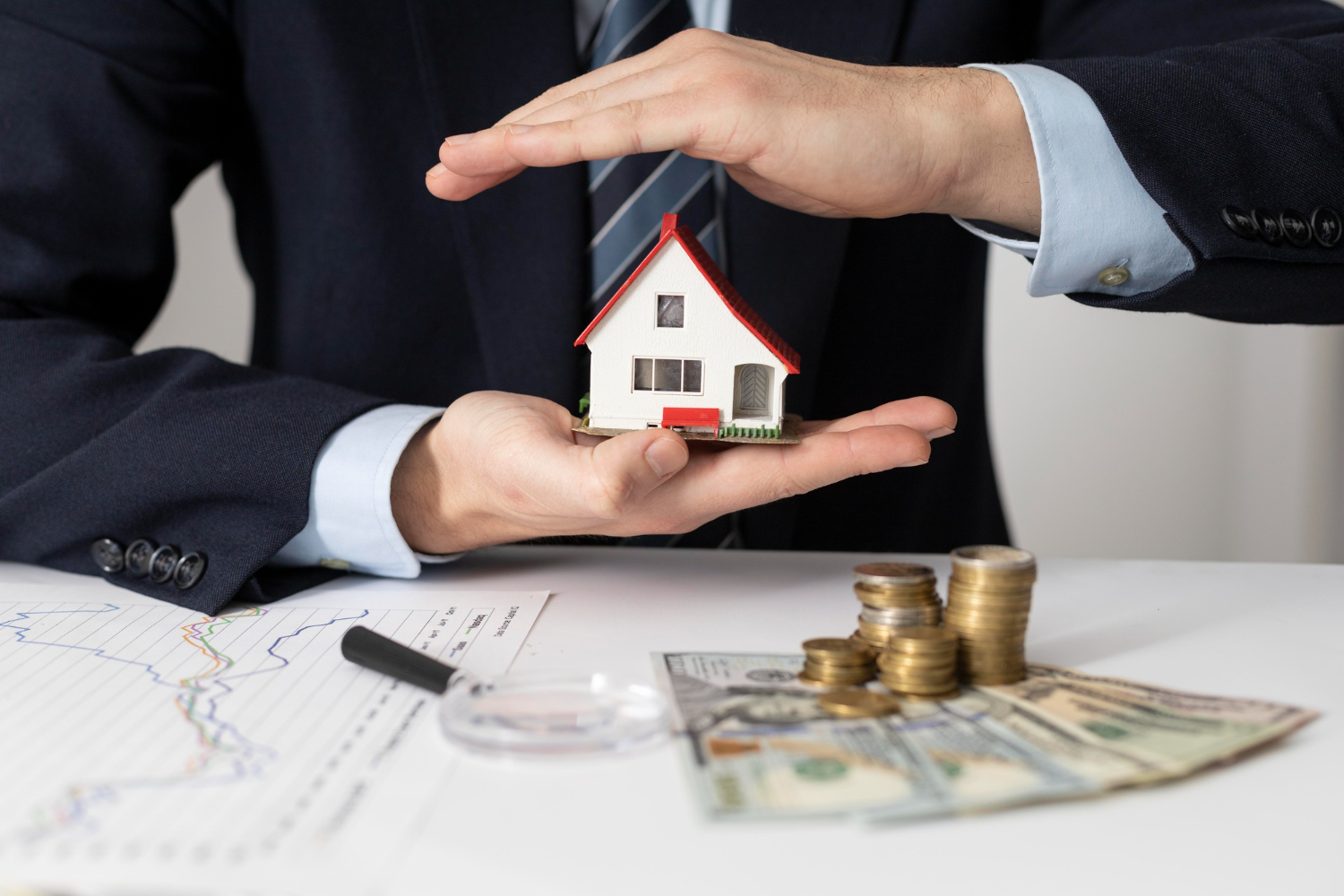 Manos sosteniendo una casa en miniatura con llaves, dinero y gráficos, simbolizando un préstamo hipotecario en Panamá.