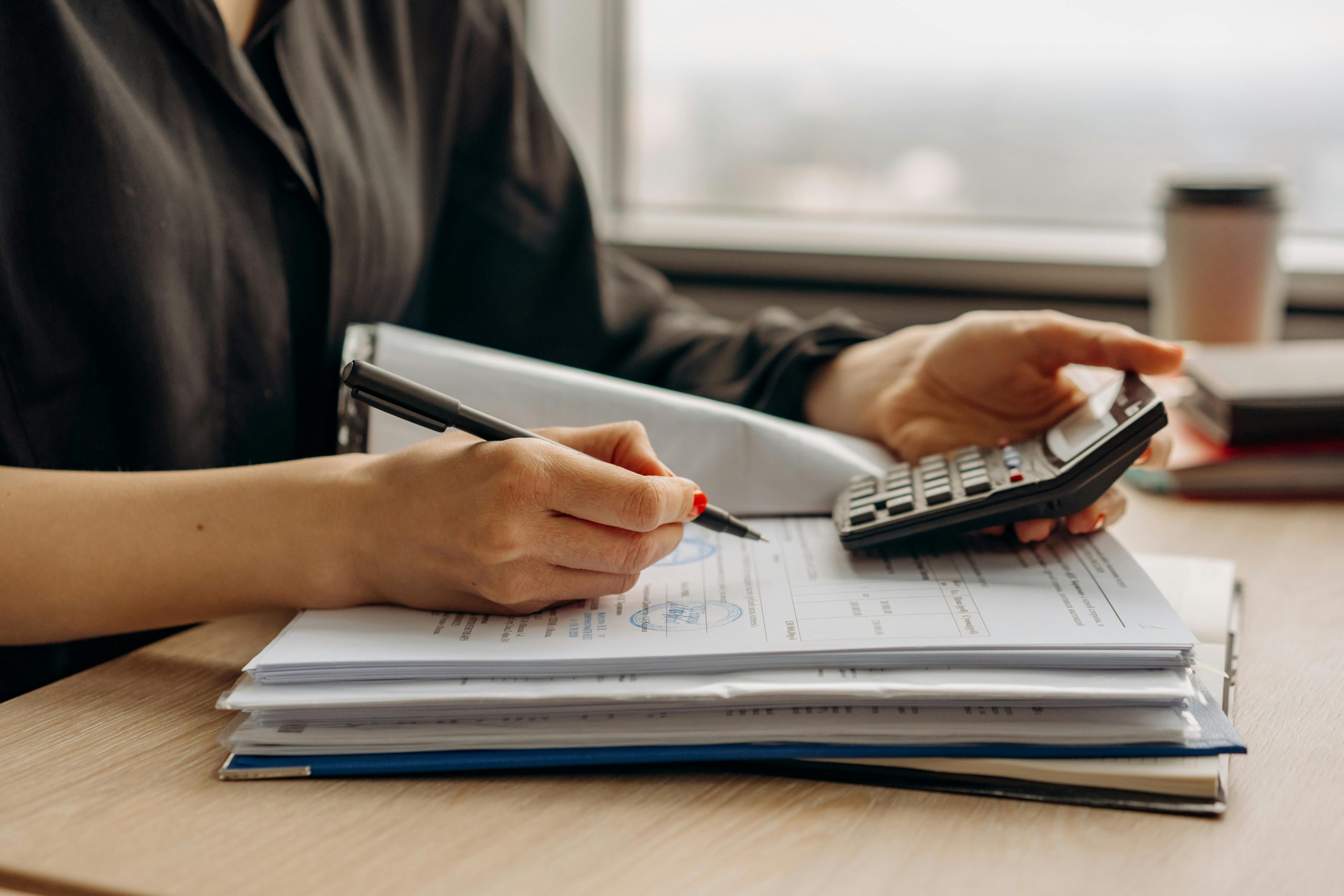 Manos calculando pagos y revisando reportes financieros con una calculadora.