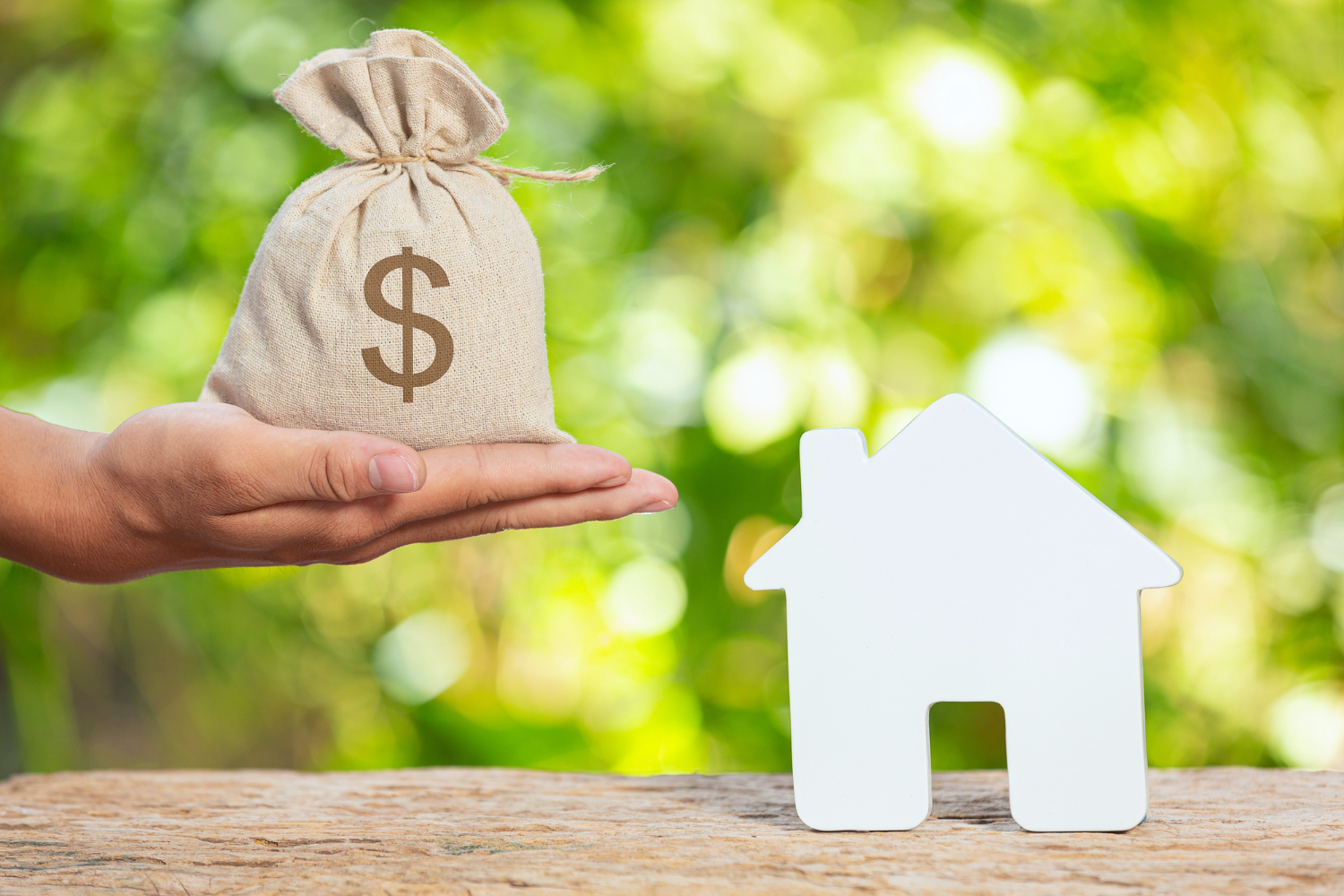Mano con bolsa de dinero y maqueta de casa